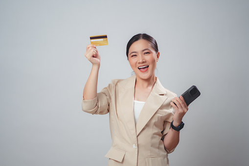 Asian woman happy excited using smart phone and credit card for shopping online standing isolated over white background.