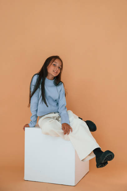 istock Sitting on white cube. Cute young girl is in the studio against background 1822286433