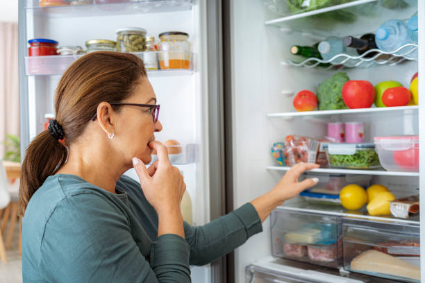 portrait of dubitative woman looking inside the fridge - esfomeado imagens e fotografias de stock