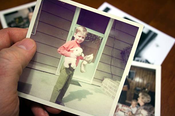 Hand holds Vintage photograph of child during summer Hand holds vintage photograph of boy in sun with pile of old photos in background. Please view my reminder photos stock pictures, royalty-free photos & images
