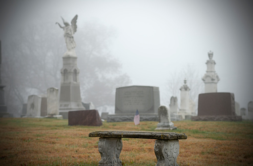 a reflection bench in a cemetery with gravestones in the background on a cold and foggy day
