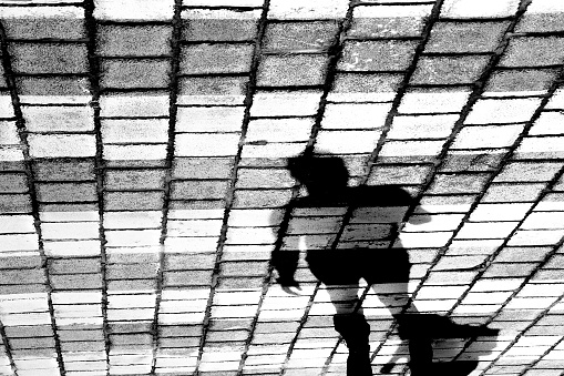 Shadow silhouette of a person crossing the cobblestone street on pelican crossing, in black and white