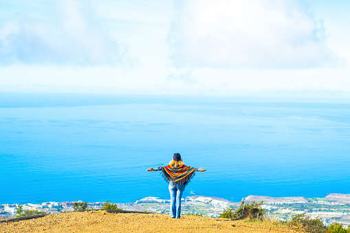 Tourist and freedom lifestyle people travel concept. Woman viewed from back opening arms to enjoy an amazing view and landscape. Blue ocean and sky from a top of a cliff. Happy lady