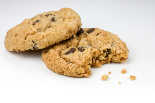 Two oatmeal chocolate chip cookies with a bite taken of one. Background has gray gradient. See related cookie images