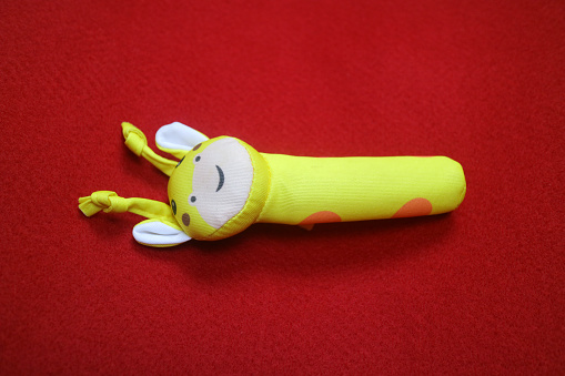 A yellow giraffe shaped baby holding toy that makes a sound when squeezed. on a red background