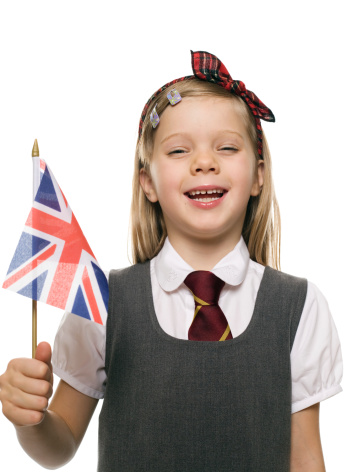 Portrait of a dressed up school girl with a bow in her hair. She's holding a British flag and laughing.