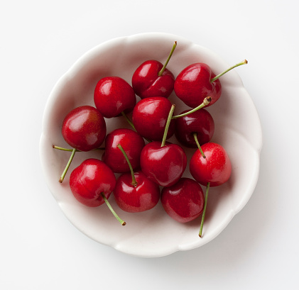 Ripe red cherries in a small white bowl, isolated on a white background