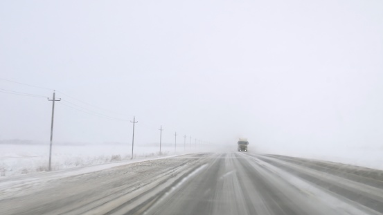 Dangerous road with ice and blizzard, clearing windshield, view from car as truck approaches. Hazardous journey on treacherous road, emphasizing risks. Confronting dangers on icy road, safety first.