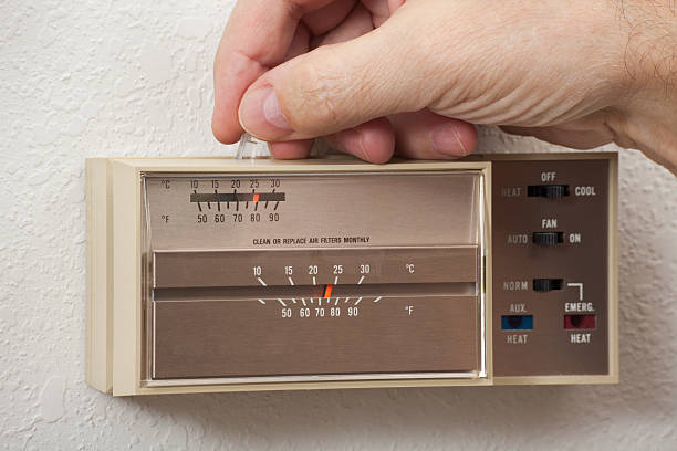 Man's hand adjusting home thermostat stock photo