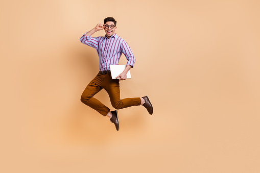 Full length photo of positive man wear trendy clothes fly air go work carry netbook macbook empty space isolated on beige color background