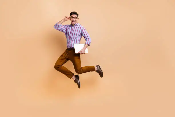 Photo of Full length photo of positive man wear trendy clothes fly air go work carry netbook macbook empty space isolated on beige color background