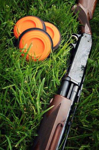 Shotgun sitting in the grass next to three clay pigeon targets.