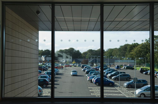 Looking out the window of a modern office building to the car park. Space for copy.