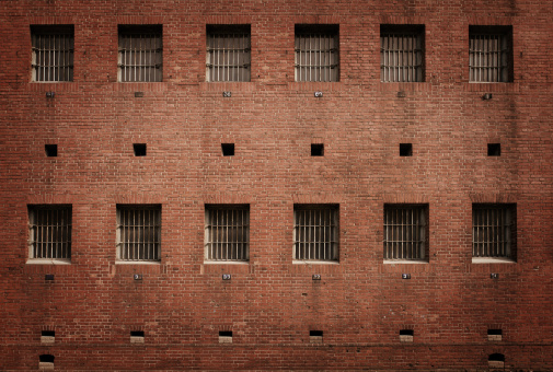 Two arched windows with metal bars and white edging on an old red brick wall. From the Windows of the world series.