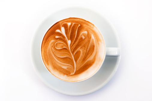 A flat white coffee with leaf pattern from above on white background.