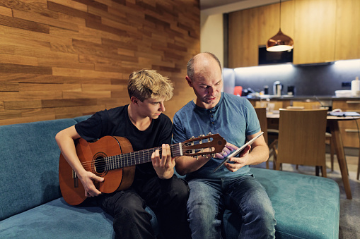 Father and teenage son playing guitar at home. The man is helping the son with practicing the chords.
Shot with Canon R5