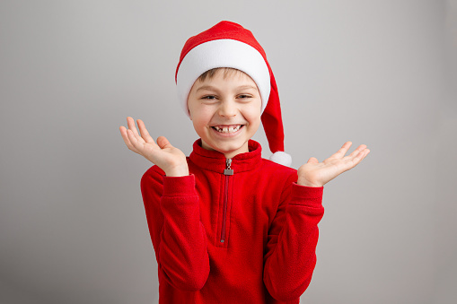 Cheerful boy in Santa hat on isolated gray background showing different funny emotions, surprise, joy, delight. Merry Christmas concept.