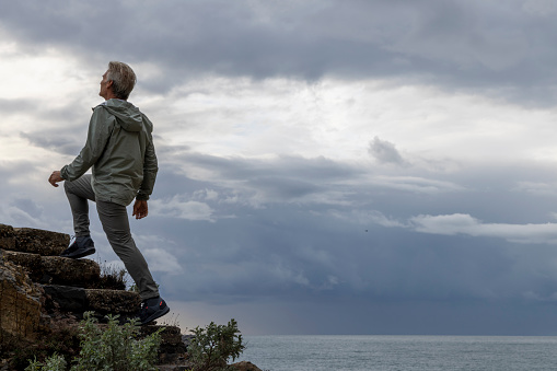 Mature man climbs steps above sea and stormy clouds