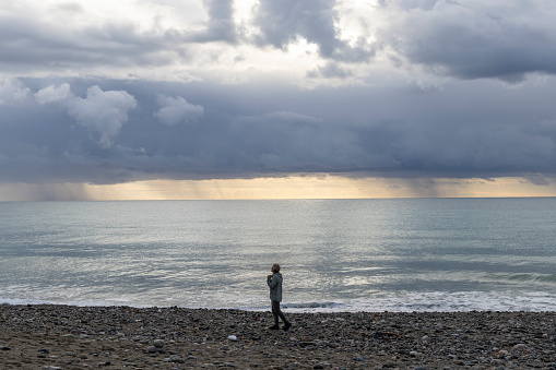 Man walks along empty beach below dramatic clouds