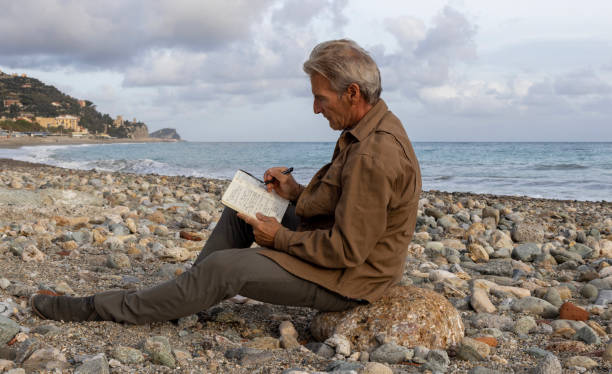 Senior man writes in journal on rocky beach