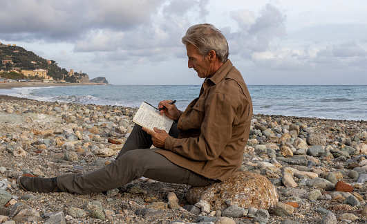 Senior man writes in journal on rocky beach