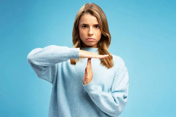 Portrait of serious woman showing timeout with hands, gesturing, looking at camera isolated on blue background. Gesture communication concept
