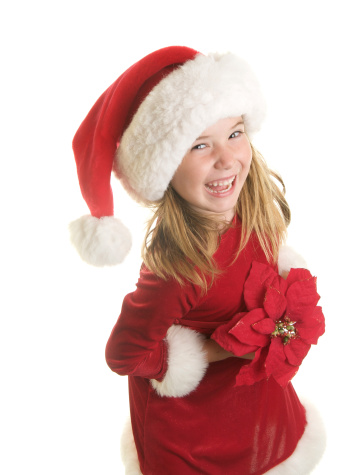 An adorable six year old girl with a Santa Claus dress and hat on.  She's holding a large artificial poinsettia flower and smiling at the camera on a white background.