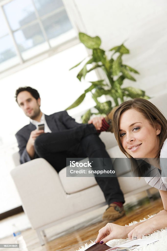 Atractiva pareja en su casa de la revista de lectura de mujer en la parte frontal - Foto de stock de 25-29 años libre de derechos