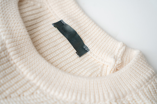 Clothing tag close-up, blank clothing label on the beige knitted sweater