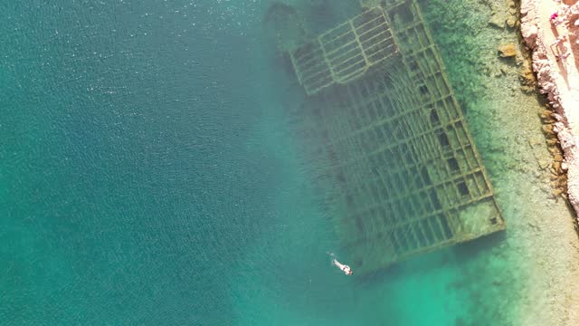 Ascending drone footage of woman swimming over the German Wehrmacht shipwreck in Zavratnica, Croatia