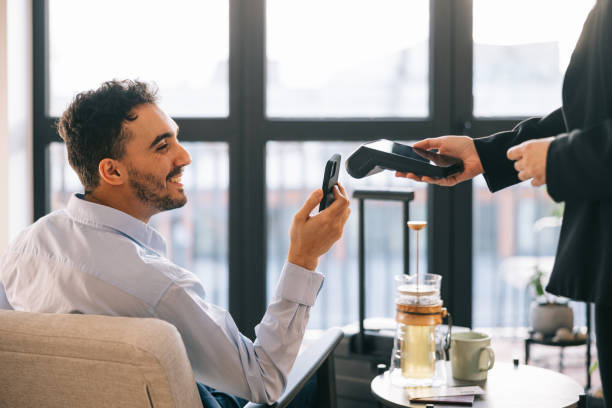 Businessman paying with smartphone in airport business lounge Businessman pays for his tea using contactless payment in the airport VIP lounge contactless airport stock pictures, royalty-free photos & images