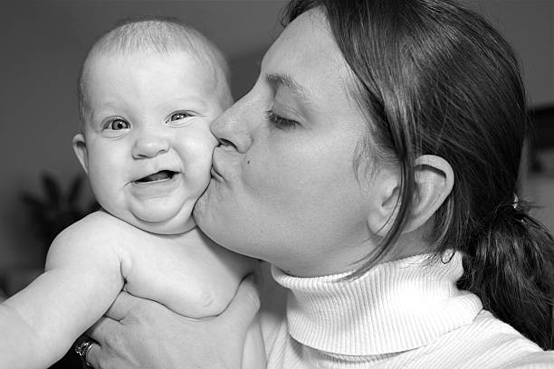 Photo taken in the 80s: Hispanic young mother posing holding her son looking at the camera at her home kitchen