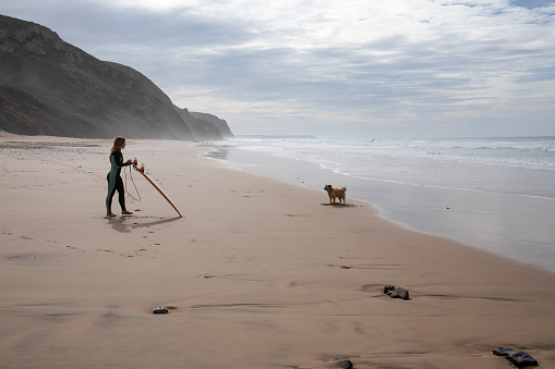 Young woman surfer relaxes on beach with dog
