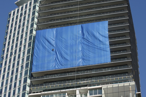 A rectangular blue tarp drapes one side of a modern apartment tower.Add your own message on the tarp.