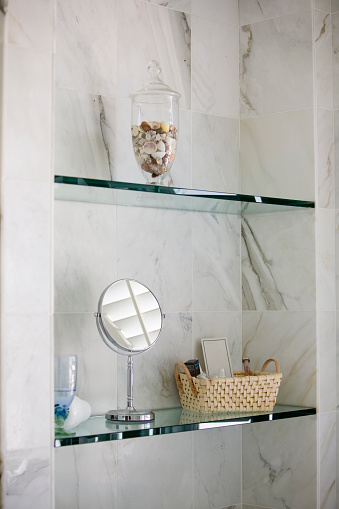 Close-up on glass bathroom shelves in marble inset with fancy bathroom accessories.