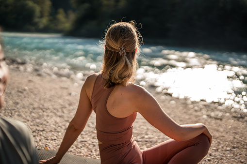 A beautiful Caucasian female sitting and stretching on a yoga mat by the soothing Soča river.