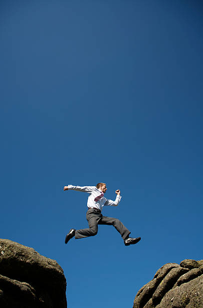 istock Businessman Leaping Outdoors in Blue Sky between Rocks 182248341