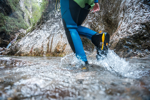 An unrecognizable person, clad in a neoprene suit and safety helmet, walks through water canyons, embracing the thrill of a canyoning adventure.