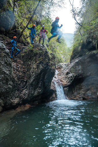 Friends of different ethnicities, in neoprene suits and safety helmets, jump into the water for an adrenaline-fueled canyoning experience.