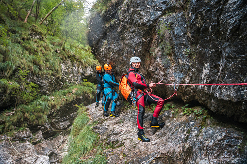 A skilled Caucasian guide leading a diverse group of friends conquering canyoning challenges, all dressed in neoprene suits and safety helmets.
