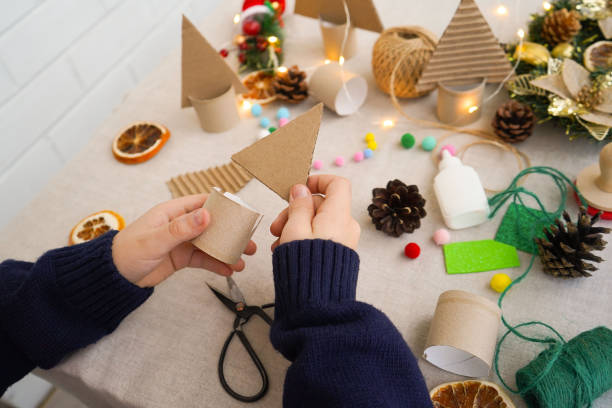 Step-by-step instructions on how to make a Christmas tree out of cardboard. Step 2 connect the upper triangular part with a cardboard roll stand. Zero waste concept.