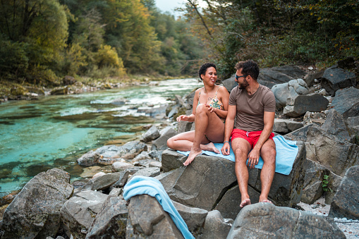 Mid adult multi-ethnic couple taking and enjoying a relaxing day by the river. They are wearing swimsuits.