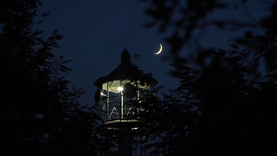 Lighthouse in the forest at night with the moon in the sky