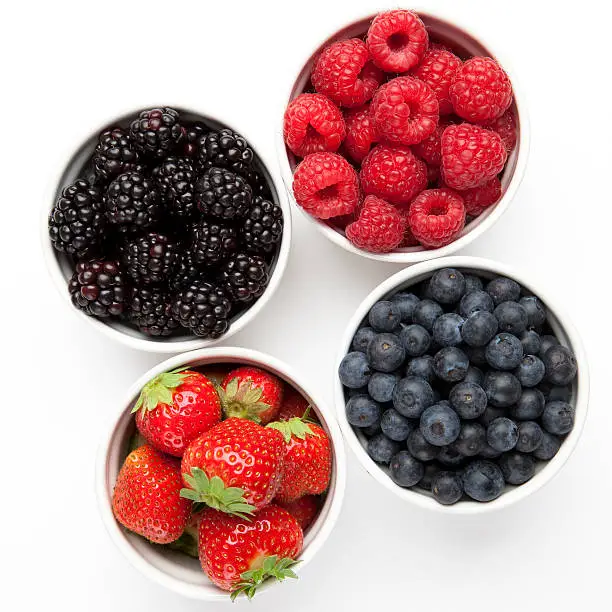 "Blackberries, raspberries, strawberries and blueberries in white bowls"