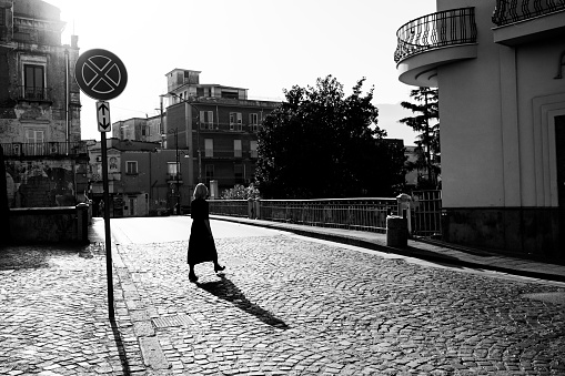 Woman crossing a cobbled street early on a Sunday morning in the town of Scafati, south of Naples, Italy.