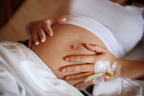 Pregnant woman holding her belly, attached to medical tubes stock photo