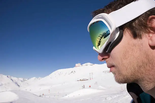 Sideview of Freestyle Snowboarder inbetween Mountains during Wintertime. Superb Mountain Range reflecting perfectly on Skiing- Goggles.