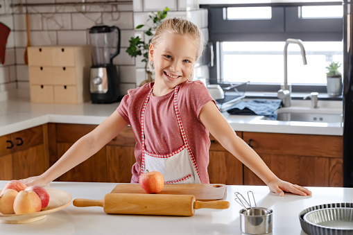 Portrait of a cute little girl in a home kitchen checking ingredients for a homemade apple pie recipe