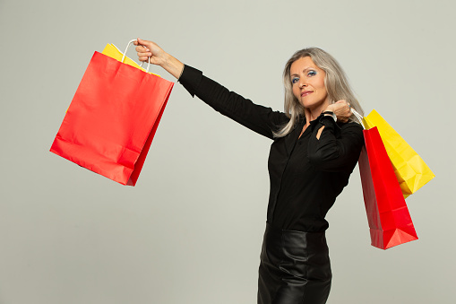 Elderly gray-haired woman with shopping, gift bags isolated on a gray background.