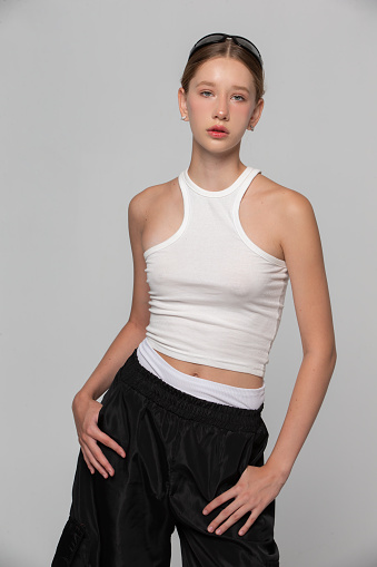 A young beautiful girl fashion model in a white top is posing on a gray background.